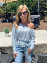 Woman wearing sunglasses and a light blue off-shoulder top outdoors
