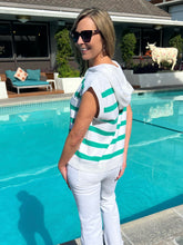 Woman in a striped shirt and sunglasses standing by a pool with a house and garden in the background.