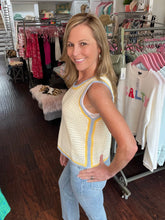 Woman wearing a yellow sleeveless crochet top in a clothing store.