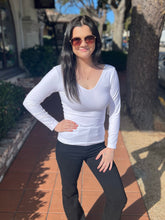 Woman wearing a white long-sleeve top and black pants standing on a sidewalk.