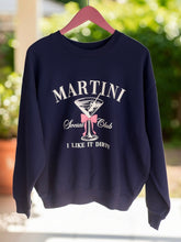 Navy blue sweatshirt with 'Martini Social Club' design on a hanger outdoors.