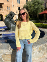Woman in a yellow sweater and blue jeans standing in front of a sculpture by a pool.