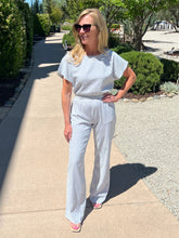 Woman in a light blue outfit standing on a sidewalk with greenery in the background