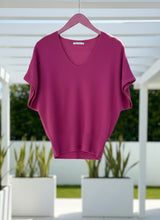 Magenta sweater on a hanger with a blurred outdoor background