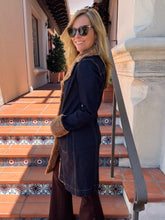 A woman wearing a dark navy blue coat with brown faux-fur trim and sunglasses, standing on terracotta tiled outdoor stairs.