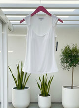White sleeveless top on a hanger with plants in the background