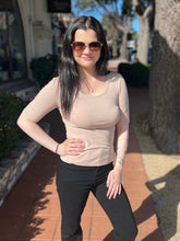 Woman wearing a khaki tee and black pants standing outdoors on a sunny day.