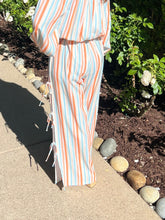 Person wearing a striped outfit standing on a sidewalk with plants and stones in the background