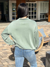 Person wearing a green sweatshirt and blue jeans standing outdoors on a patio.