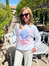 Woman wearing a white sweatshirt with a shell design and 'Summer Vibes' text, sitting outdoors.