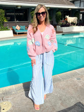 Woman in a pink floral cardigan and striped pants standing by a pool.