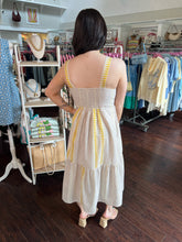 Woman wearing a white dress with yellow accents in a clothing store.