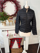 Black puffer jacket on a mannequin in front of a festive fireplace with wreath and stockings.