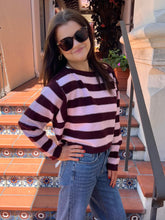 A young girl wearing a dark burgundy and light pink striped knit sweater, blue jeans, and sunglasses, posing on outdoor tiled steps.