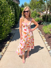 Woman in a picnic print dress standing on a sidewalk with trees and shrubs in the background