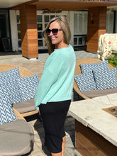 Woman in a light mint sweater and black skirt standing outdoors near outdoor furniture.