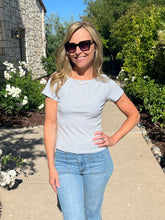 Woman wearing sunglasses and a striped shirt standing outdoors with greenery and flowers in the background