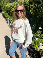 Woman wearing a white sweatshirt with a dog graphic and blue jeans, standing outdoors.