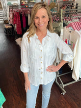 Woman in a white embroidered shirt and jeans standing in a clothing store.