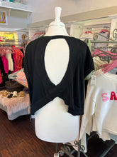Black open-back top on a mannequin in a store setting with clothing racks and shelves in the background.