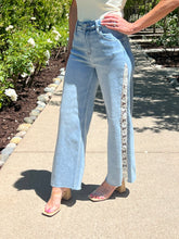 Person wearing light blue jeans with a decorative side panel on a sidewalk.