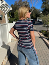 Woman wearing a striped shirt and sunglasses, standing on a sidewalk.