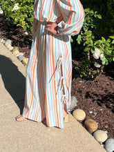 Person wearing a colorful striped outfit standing outdoors on a stone path with greenery.