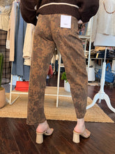 A person shown from the back wearing brown patterned cropped pants with a brown sweater and beige block-heel mules in a clothing boutique.