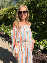 Woman in a striped top standing outdoors with greenery in the background