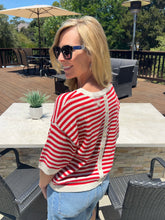 Woman wearing a red and white striped sweater and sunglasses outdoors on a patio.