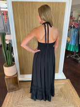 Person wearing a black dress showing the back view standing in front of a wall.