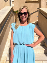 Woman in a light blue top and skirt standing outdoors on a sunny day.