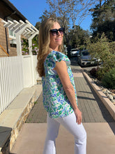 Woman wearing a floral top and sunglasses on a sidewalk with a house and trees in the background