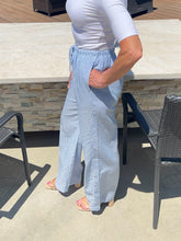 Person wearing light blue checkered pants and a white top outdoors.