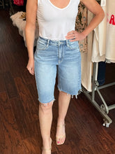 Person wearing a white tank top and light blue denim shorts in a store setting.