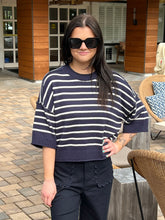Woman wearing a navy and white striped sweater and dark pants outdoors.