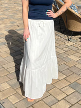 Person wearing a white skirt and navy top on a paved outdoor floor.