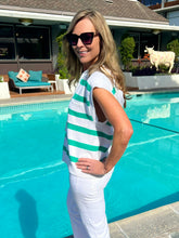 Woman in a striped shirt standing by a pool with a house and outdoor furniture in the background