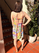 Woman in a colorful mini dress standing on a tiled patio with a plant and staircase in the background