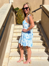 Woman in a blue patterned dress standing on stone steps outdoors.