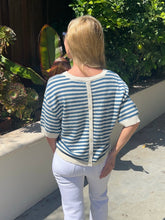Woman wearing a blue and white striped shirt and white pants standing outdoors.