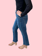Person wearing blue jeans and a black top on a pink background