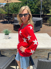 Woman wearing a red sweater with white stars outdoors on a patio.