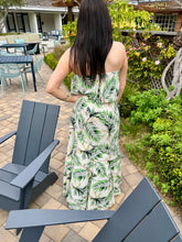 Woman in a green and white patterned dress standing in a garden setting with outdoor furniture.