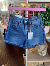 Blue denim shorts with a brand tag on a hangar hanging on a rack.