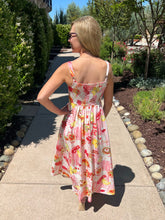 Woman in a picnic print dress standing on a sidewalk with trees and shrubs in the background