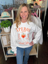 Woman wearing a white sweatshirt with orange Aperol Spritz text and graphics in a store setting