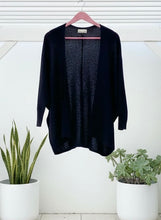 Black cardigan on a hanger with plants in the foreground