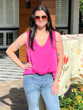 Woman wearing a pink tank top and blue jeans standing outdoors.