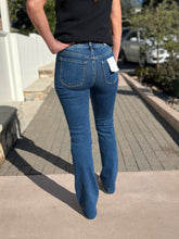 Person wearing blue slim bootcut jeans standing on a sidewalk.